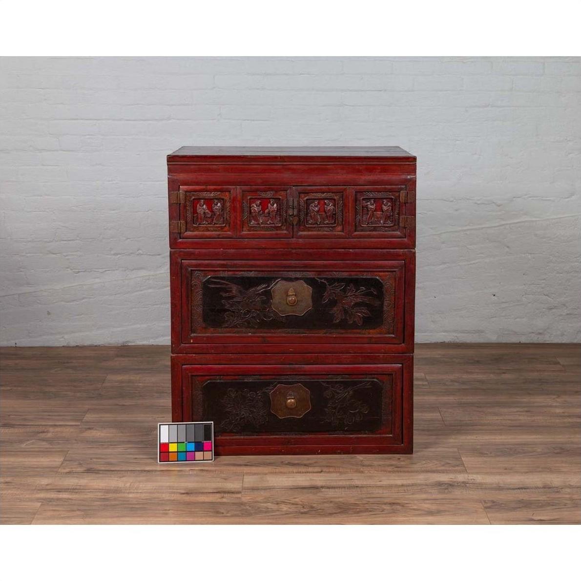 Red and black lacquered antique Chinese wooden chest with carved figures, three sections, on a wooden floor.