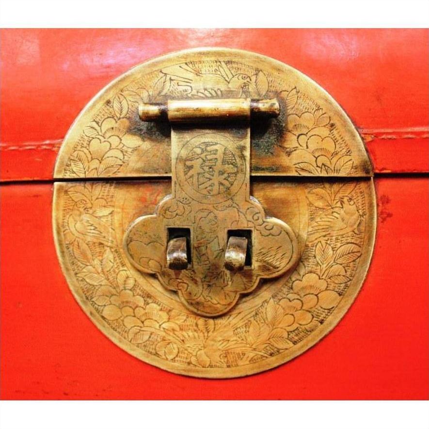 Close-up of ornate circular brass latch with floral engravings on red lacquer antique Chinese blanket chest.
