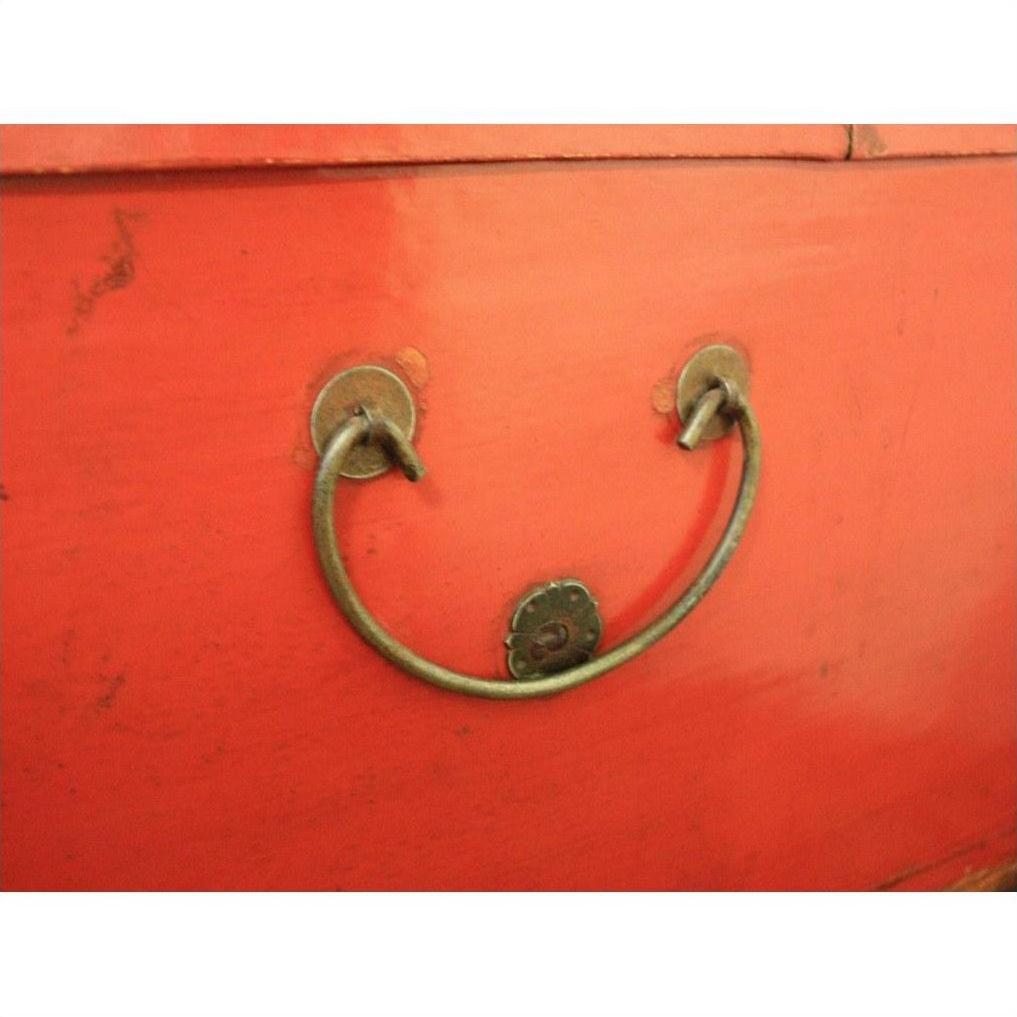 Red lacquer antique Chinese blanket chest with metal handle shaped like a smiling face, screw eyes visible.