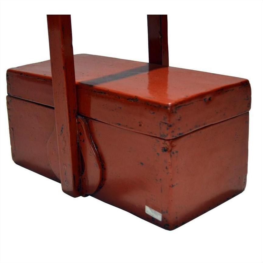 Close-up of antique Chinese red lacquer wood box with handle, showing distressed edges and visible wear.