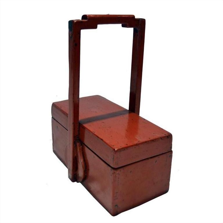 Red lacquer wood box with tall handle and two lidded compartments, antique Chinese style, close-up on plain background.