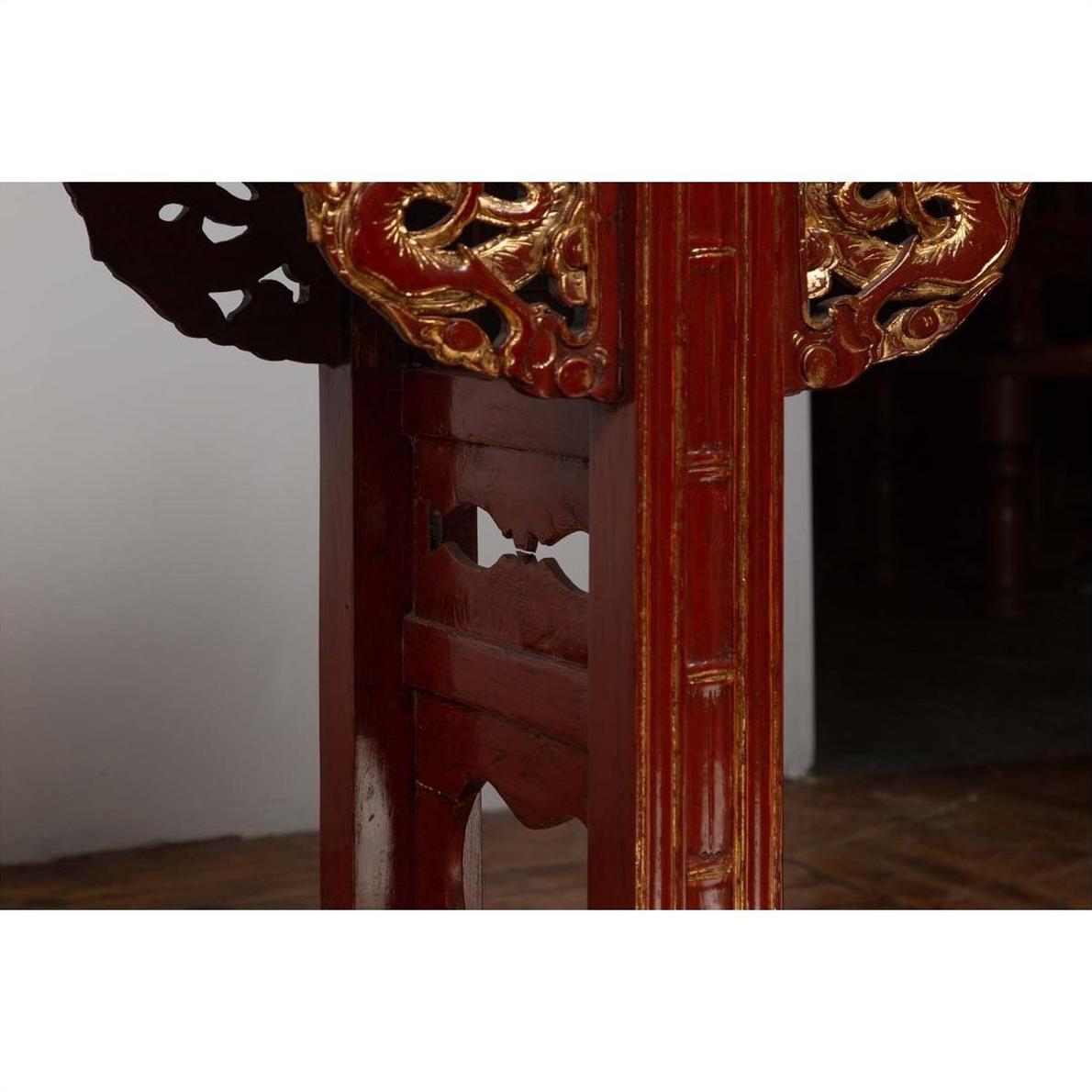 Close-up of red lacquered wood console table with carved apron and intricate decorative patterns.