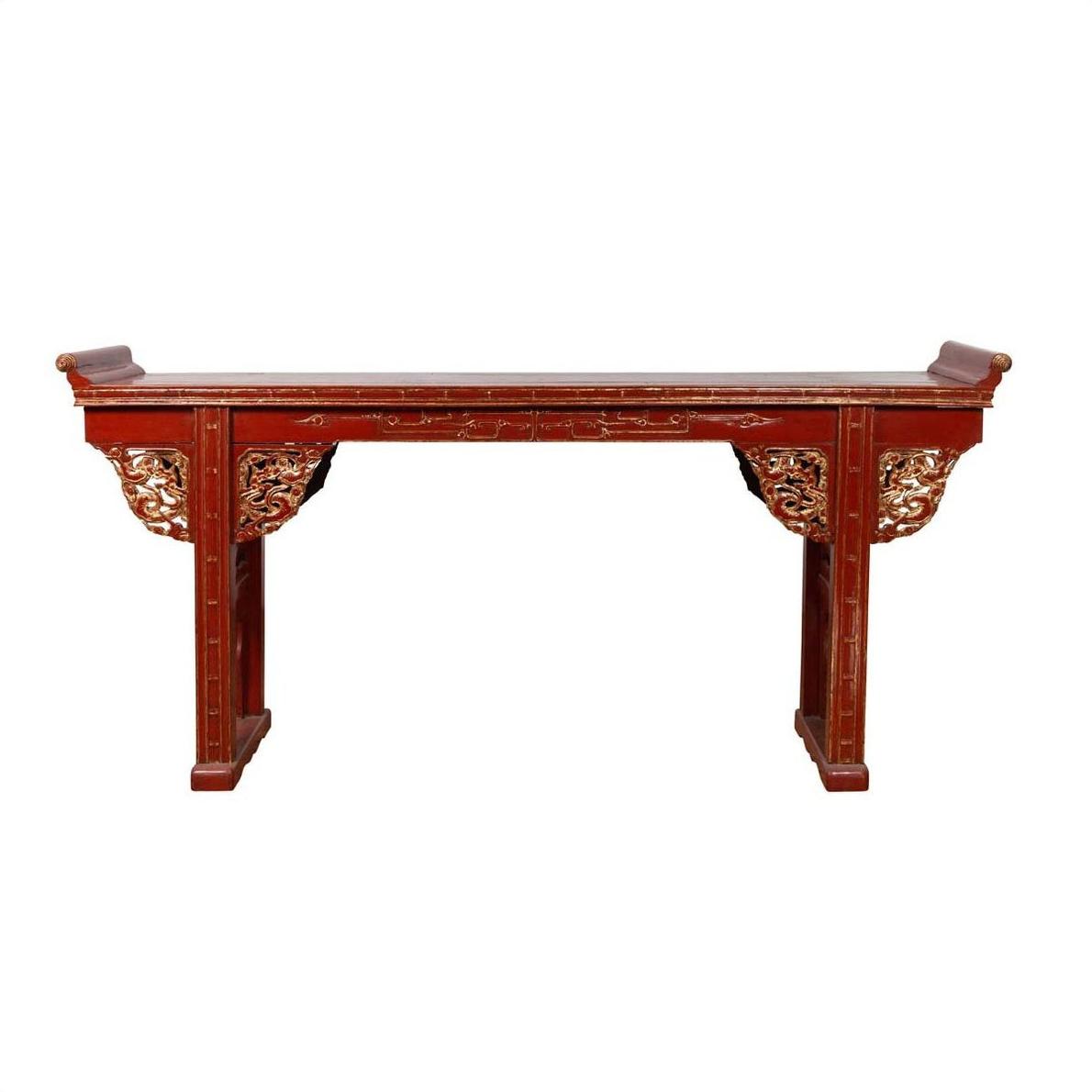 Red lacquered wood console table with carved apron against white background.