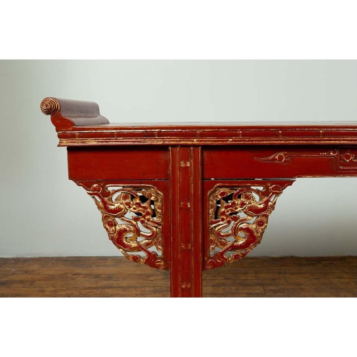 Red lacquered wood console table with carved apron and gold accents, side view.
