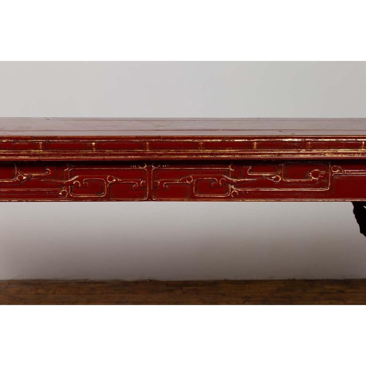 Close-up of red lacquered wood console table with carved apron, positioned indoors against a plain white wall.