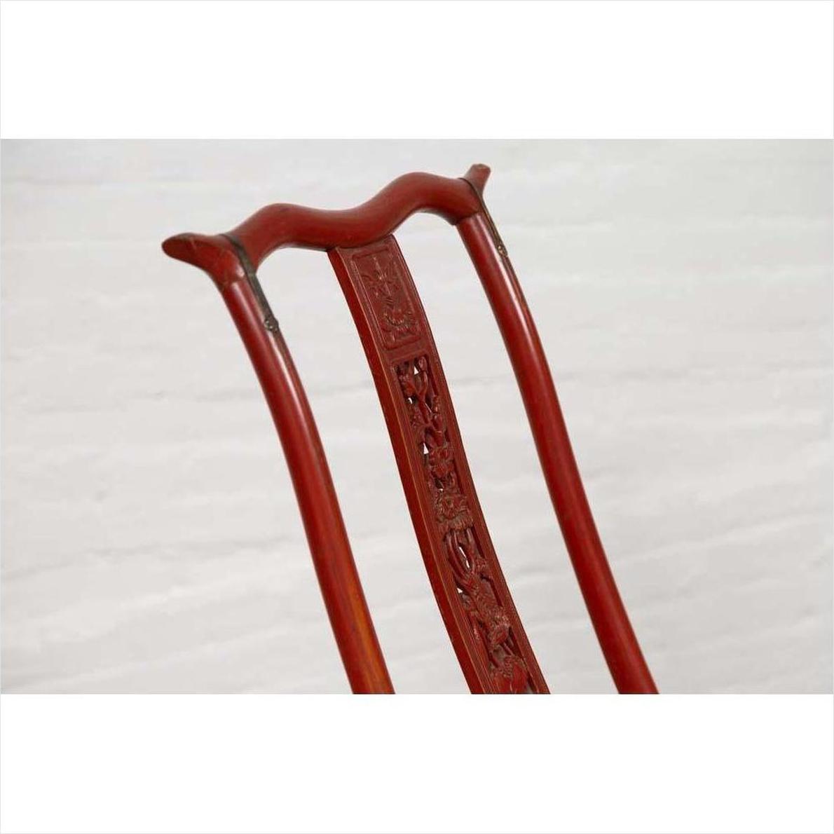 Close-up of a red lacquered wooden folding chair with carved back, footrest, and fabric upholstery.
