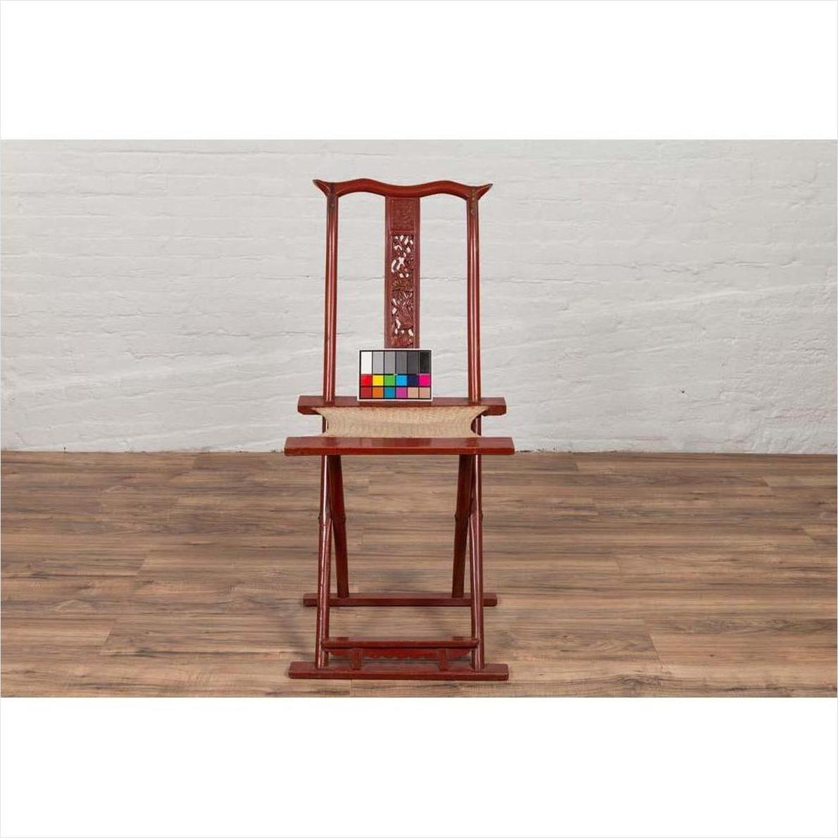 Red lacquered wood folding chair with footrest and fabric, placed on a wooden floor indoors.