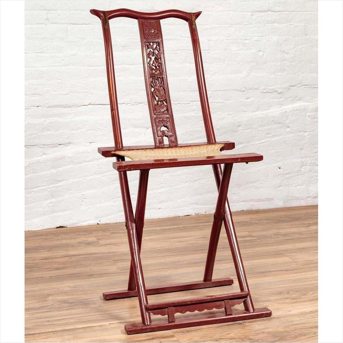 Red lacquered wood folding chair with footrest and fabric, on wooden floor by white brick wall indoors.