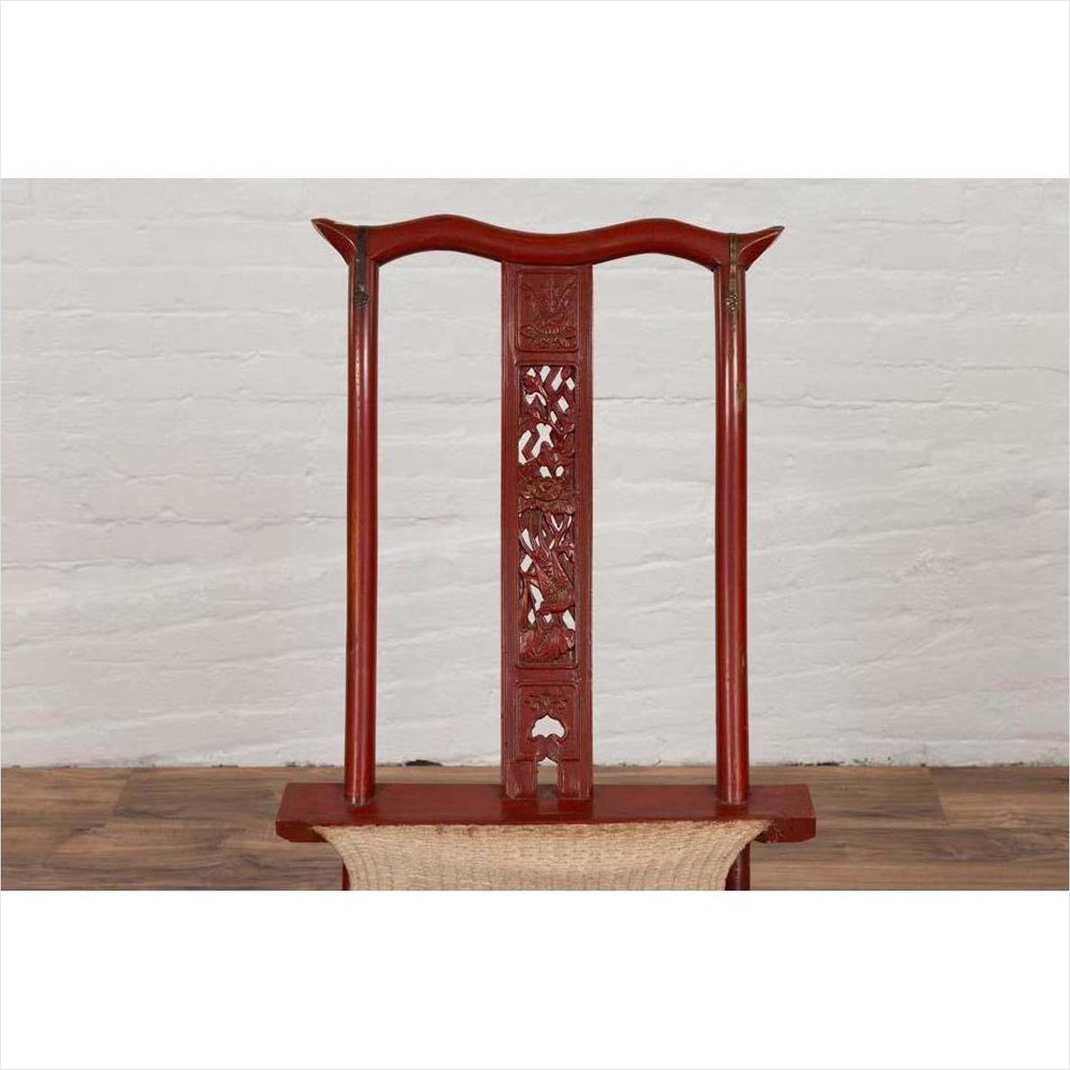 Red lacquered wood folding chair with fabric seat and footrest, indoors against white brick wall on wood floor.