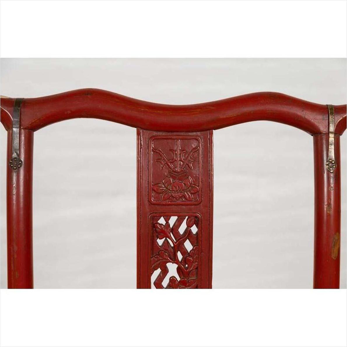 Red lacquered wood folding chair with floral carvings, footrest, fabric and metal accents, antique style.