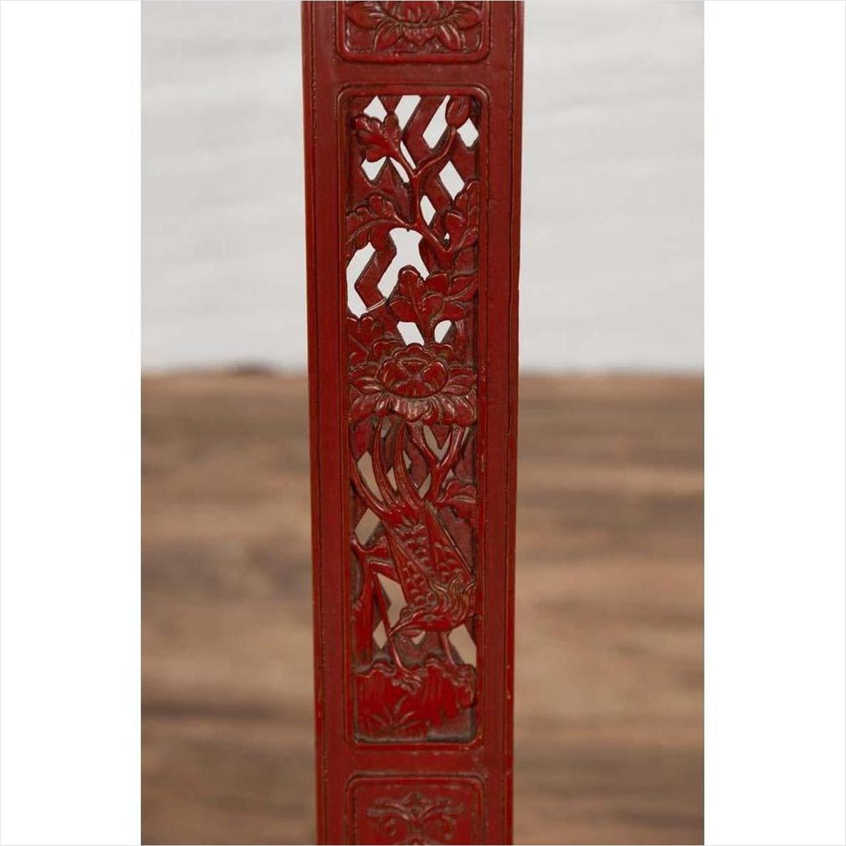 Close-up of red lacquered wood panel with carved floral and bird motifs on antique folding chair.