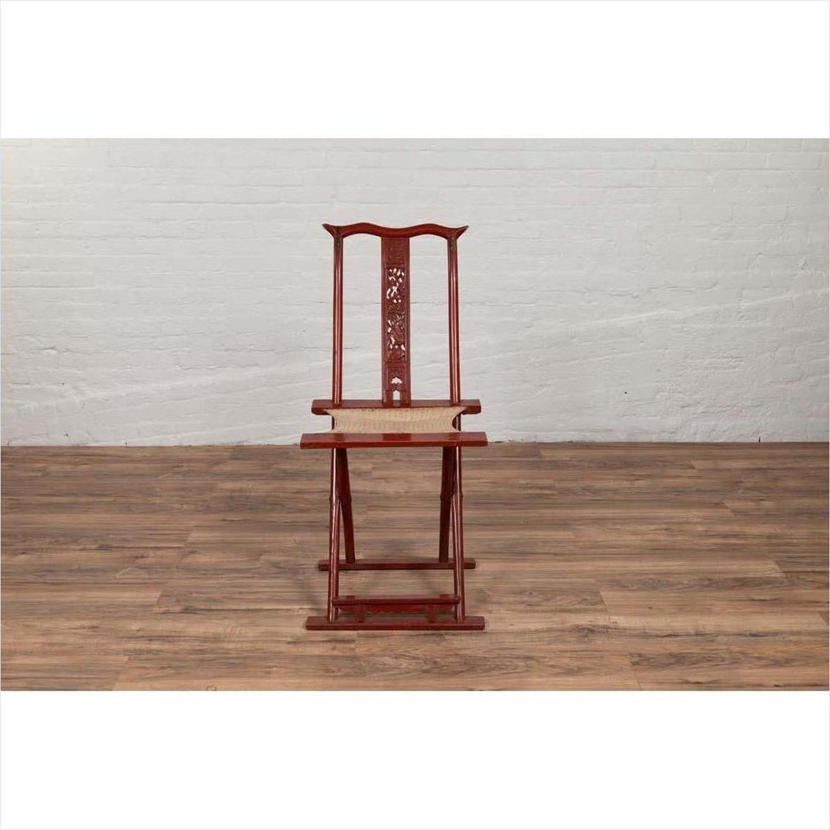 Red lacquered wood and fabric folding travel chair with footrest, indoors on wood floor against white wall.