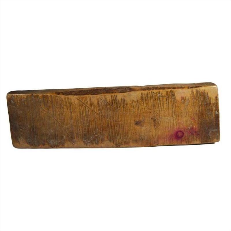 Close-up of a rectangular, worn wooden Chinese rice mold with scratches and a small purple stain on one end.