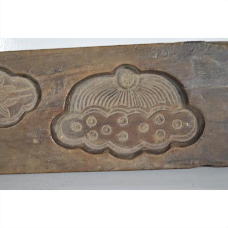 Close-up of antique Chinese rice mold, brown wood with circular top and dotted decorative patterns, on neutral background.