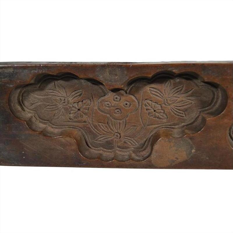 Brown wood antique Chinese rice mold with carved floral design, three flowers, leaves, and cloud-shaped border, close-up.