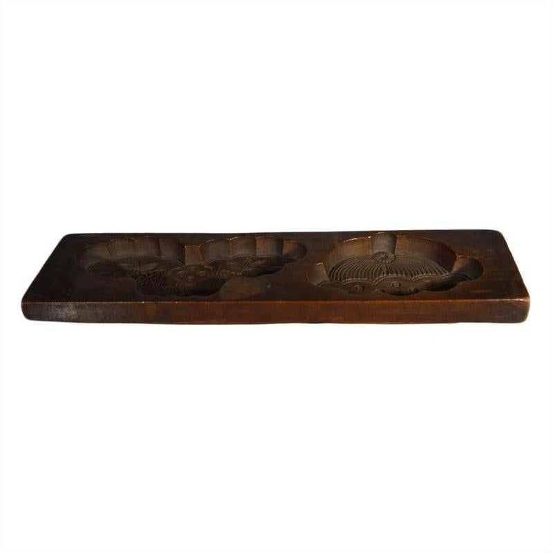Close-up of rectangular antique Chinese rice mold made of wood with two carved circles, on plain white background.