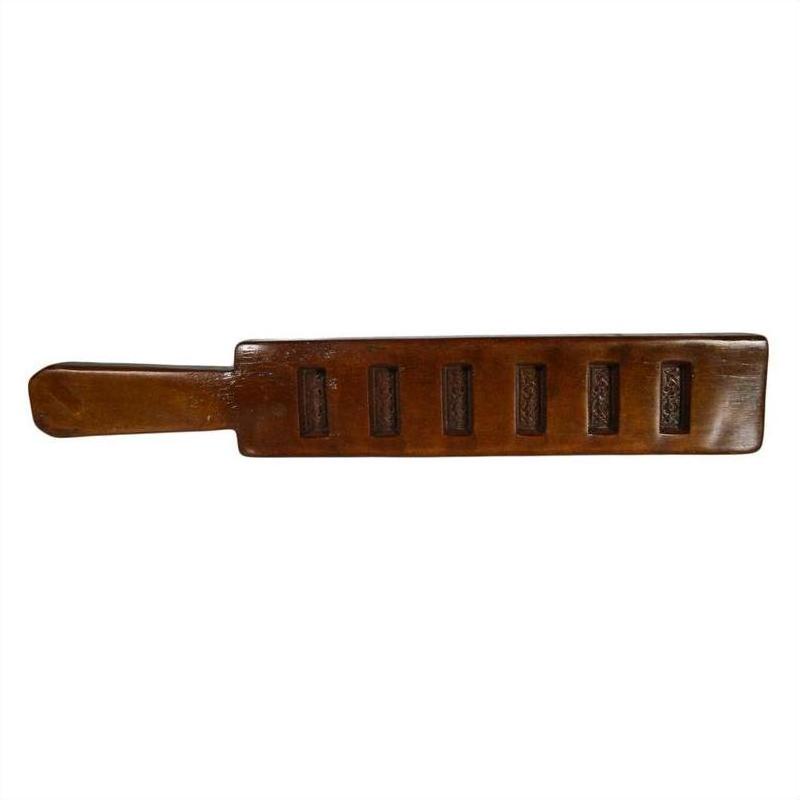 Brown wooden antique Chinese rice mold with a handle and six slotted openings, close-up on a plain background.