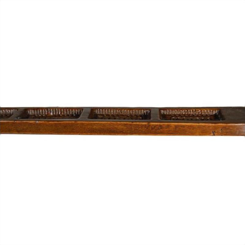 Brown wooden antique Chinese rice mold with four compartments and vertical spikes, close-up on a plain surface.