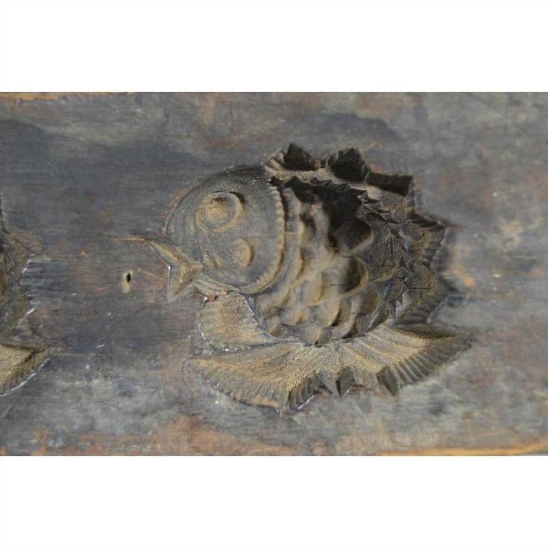 Close-up of dark, weathered antique Chinese rice mold with detailed fish carving, wood surface visible.