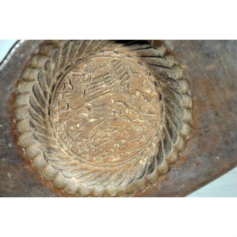 Close-up of a weathered antique Chinese rice mold with a round motif and braided rim on a textured surface.