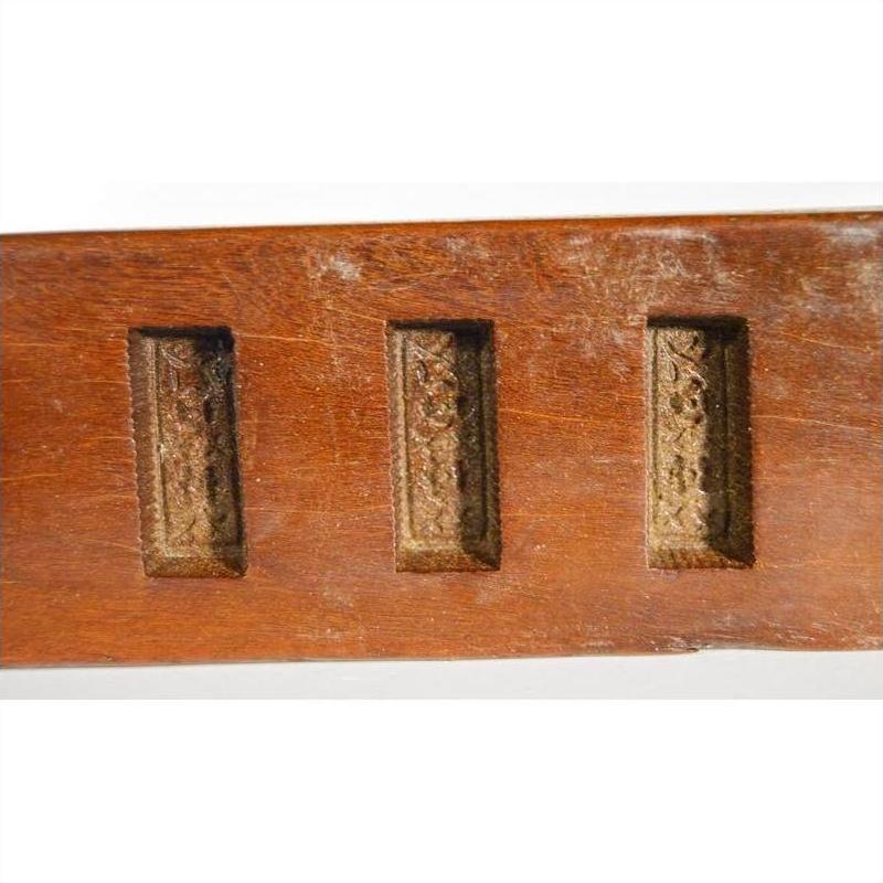Close-up of antique wooden Chinese rice mold with six rectangular motifs and incised characters, neutral background.
