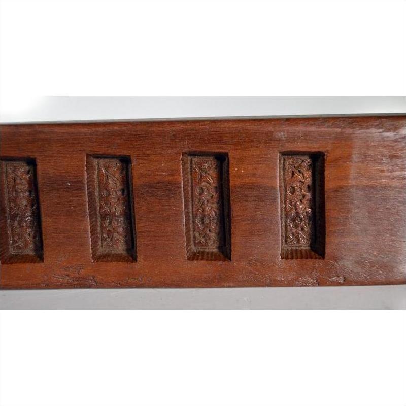 Close-up of brown antique wooden Chinese rice mold with six carved character cavities and curved paddle shape.