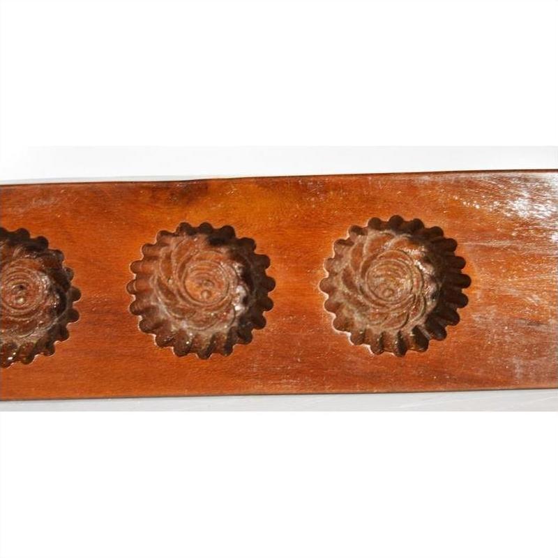 Close-up of antique wooden Chinese rice mold with four rosette cavities and a long handle, on a plain background.