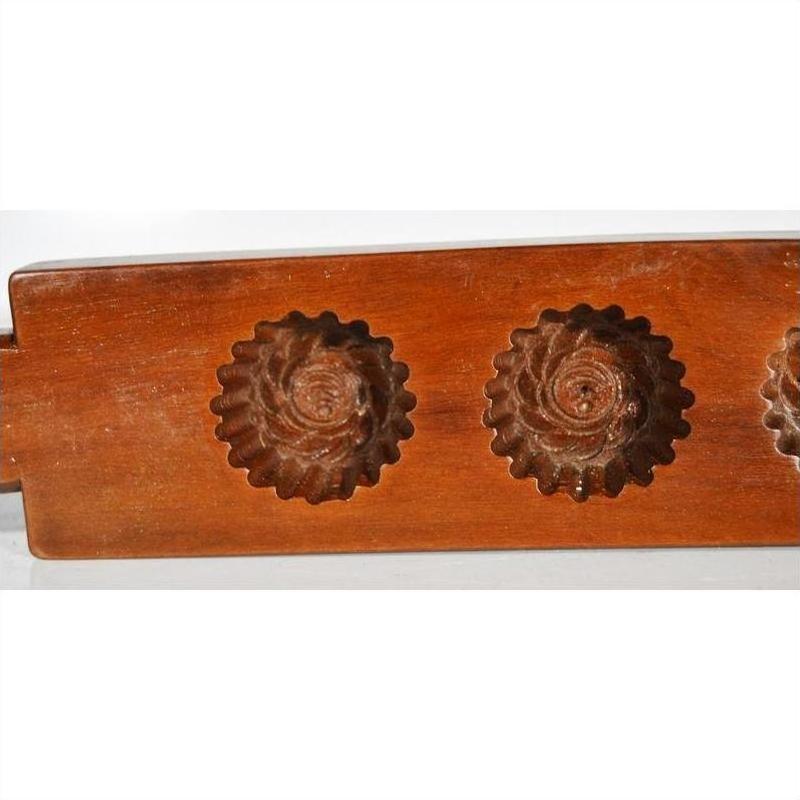 Brown wooden antique Chinese rice mold with four rosette cavities and a long handle, close-up on plain background.