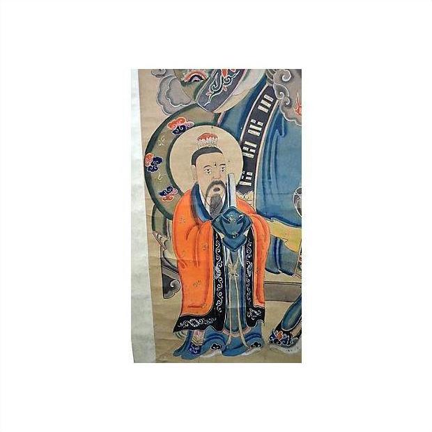 Close-up of antique Chinese scroll painting showing bearded man in orange robe with blue scarf, decorative background.