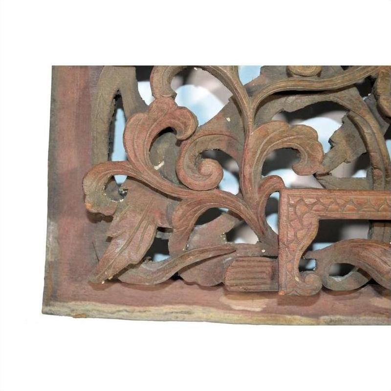 Reddish-brown wood temple carving with intricate floral and leaf designs, close-up.