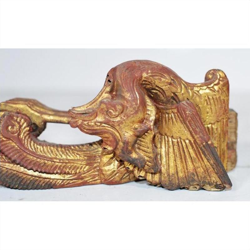 Close-up of gold and red antique Chinese temple carving with bird-like wing and elongated, curved head design.