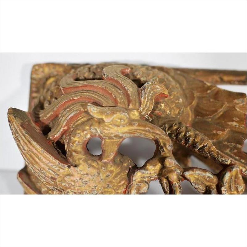 Close-up of gold and red wooden phoenix carving with intricate feather patterns, antique Chinese temple art.