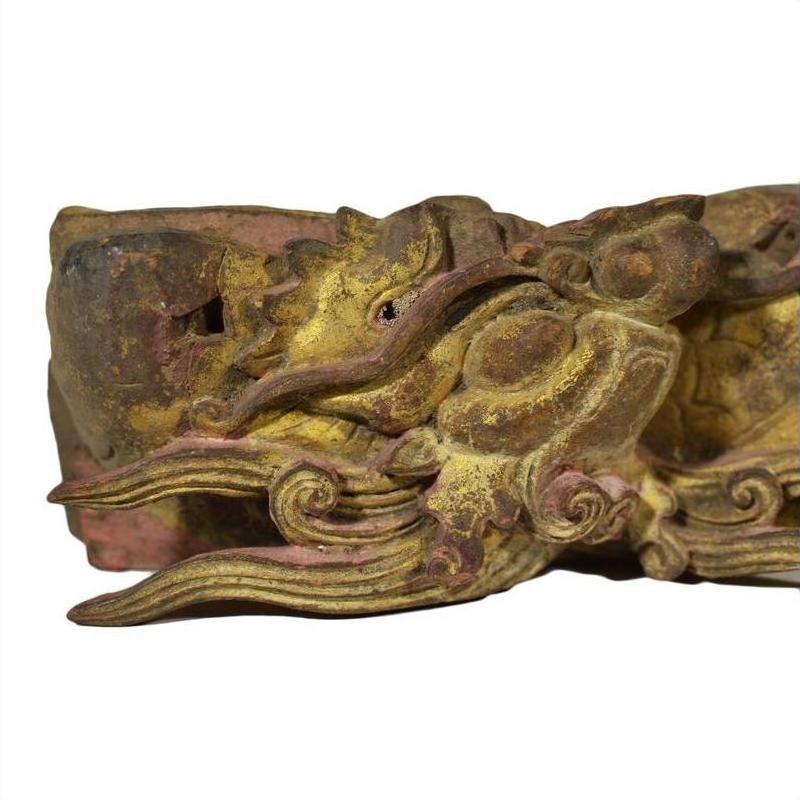 Close-up of antique Chinese temple carving featuring intricate dragon design, weathered wood, and faded gold-red paint.