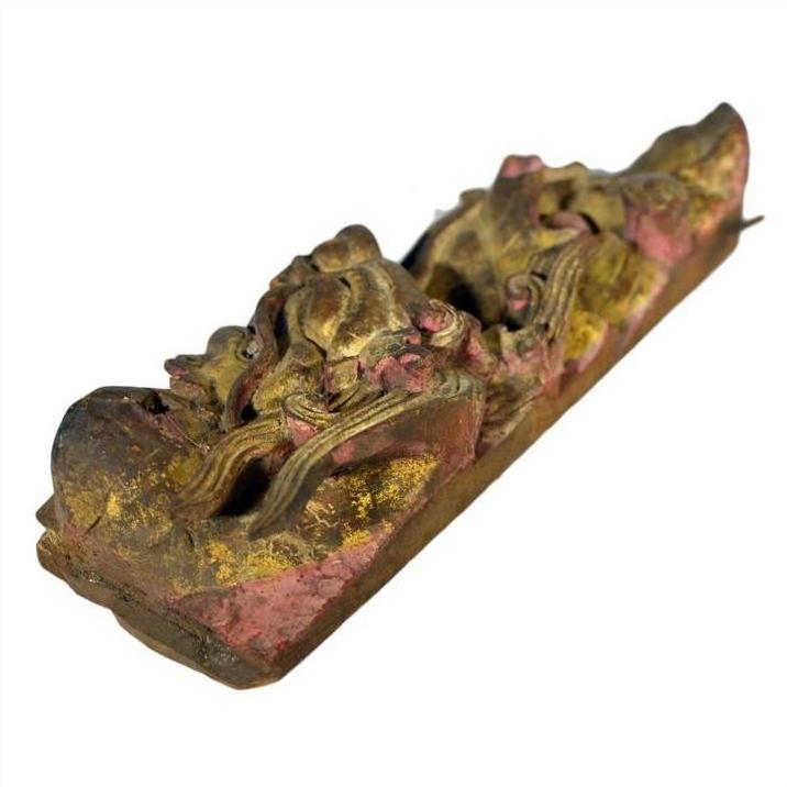 Close-up of antique Chinese temple carving in weathered gold and red wood with ornate swirling vintage patterns.