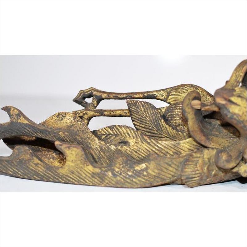 Close-up of gold leaf wood Chinese temple carving with ornate scroll patterns against a plain background.