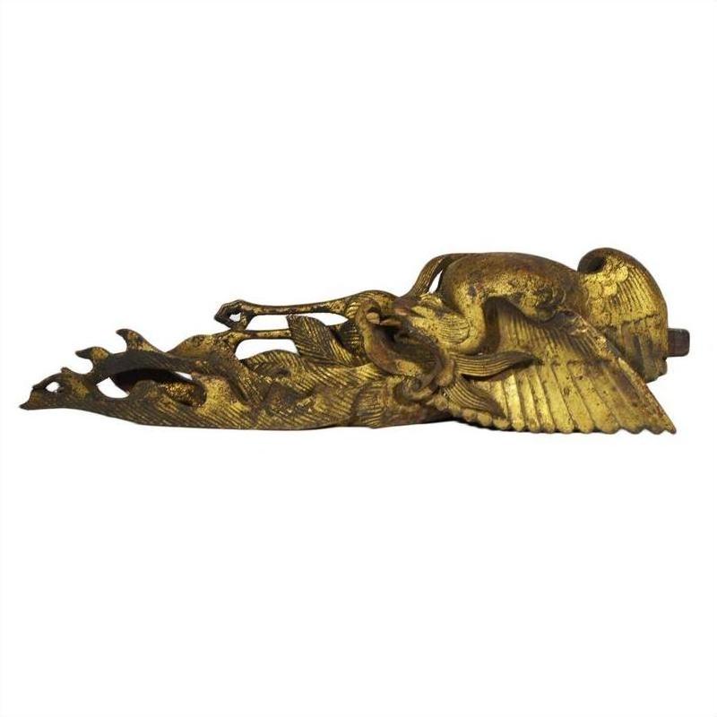 Close-up of a golden intricately carved antique Chinese temple crane sculpture resting on its side against a plain background.