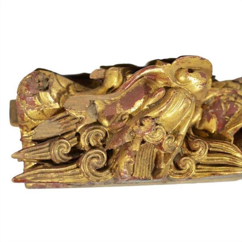 Gold and red wood temple carving with bird among swirling clouds, intricate detailing, close-up view.