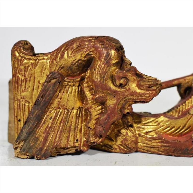 Close-up of gold and red wood griffin carving with intricate wings and lion-like face from antique Chinese temple.