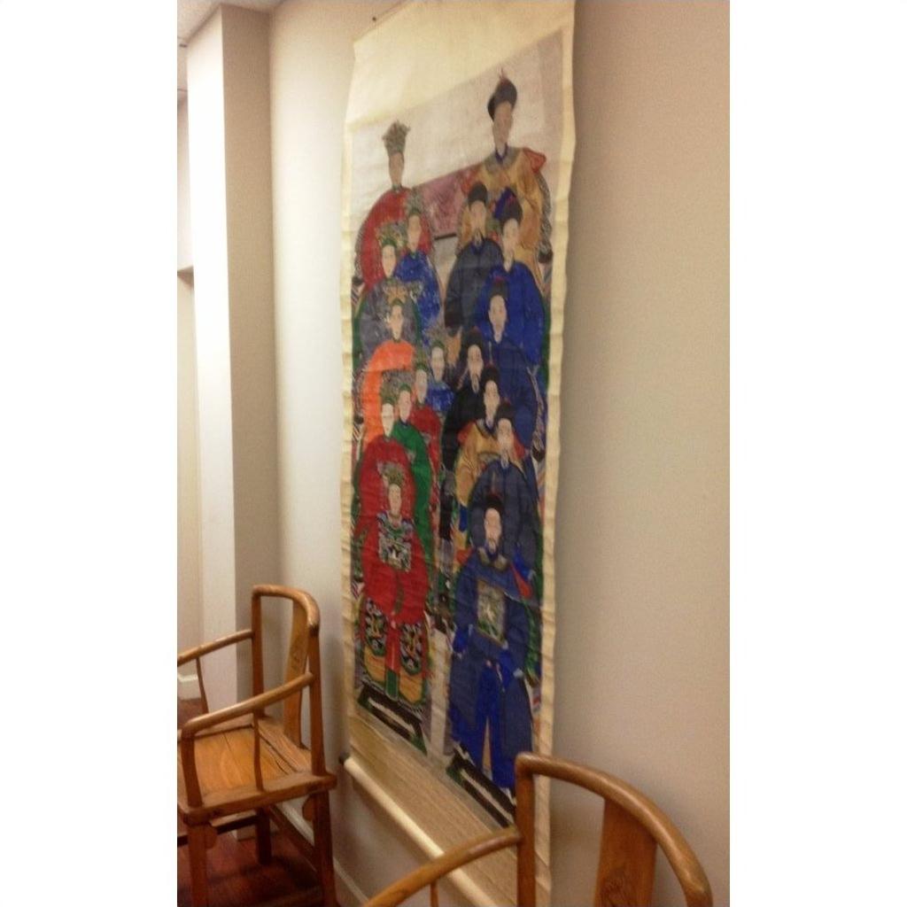 Antique Chinese silk wall hanging in neutral tones displayed between two wooden chairs against a plain wall.