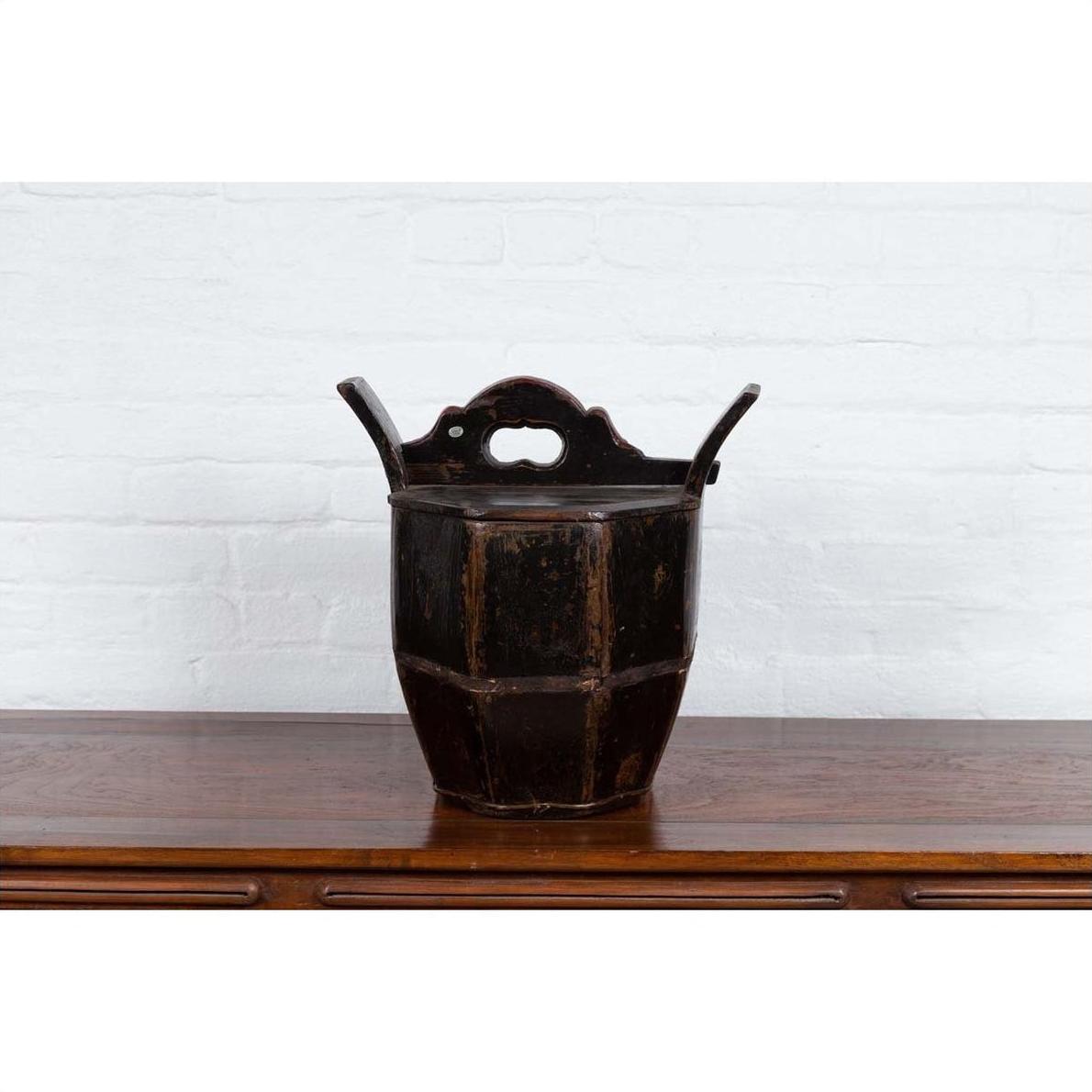 Brown wooden Chinese wedding box with carved handle, animal and foliage motifs on a wooden table against white brick wall.