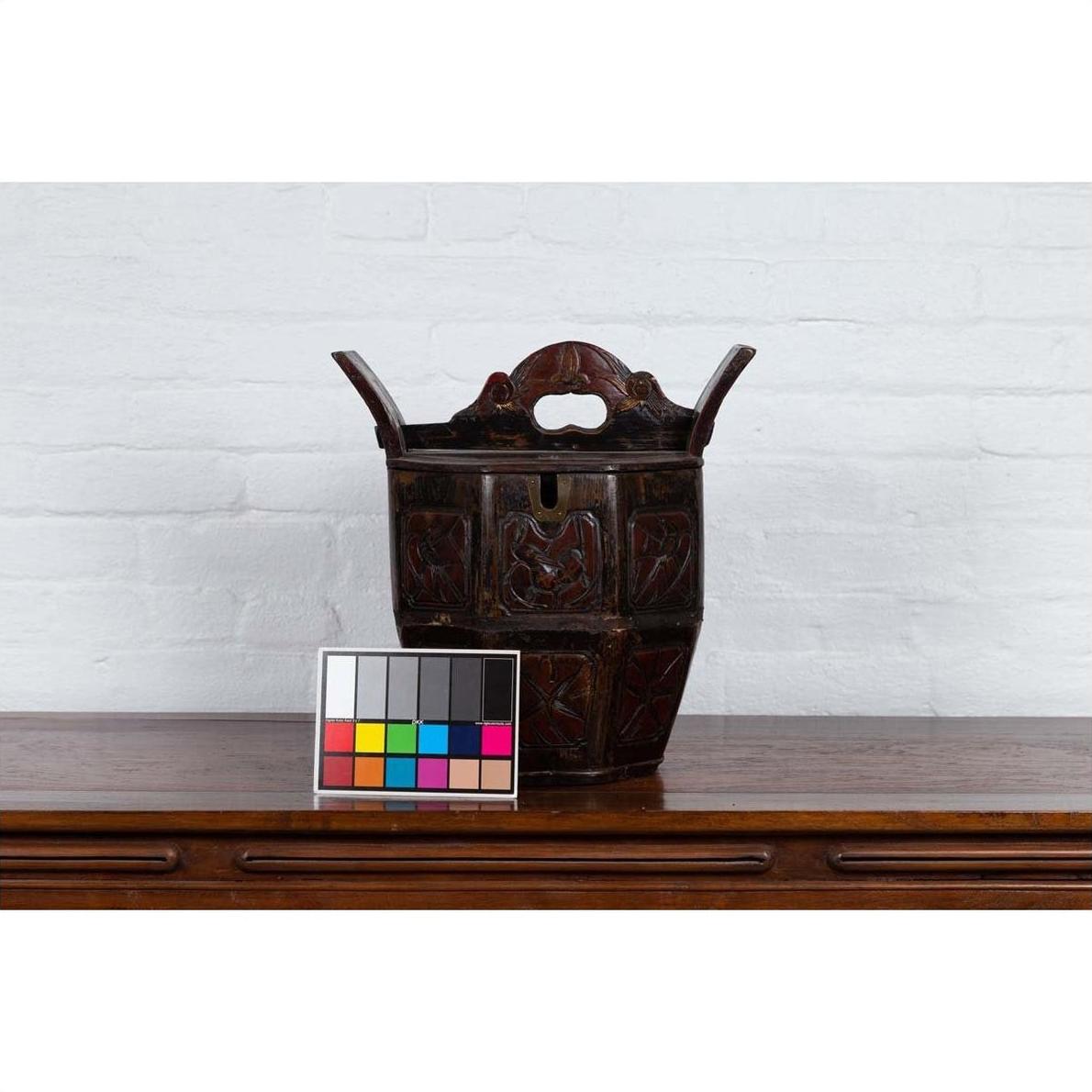 Brown wood Chinese wedding box with carved handle, animal and foliage motifs, on wooden table against white brick wall.