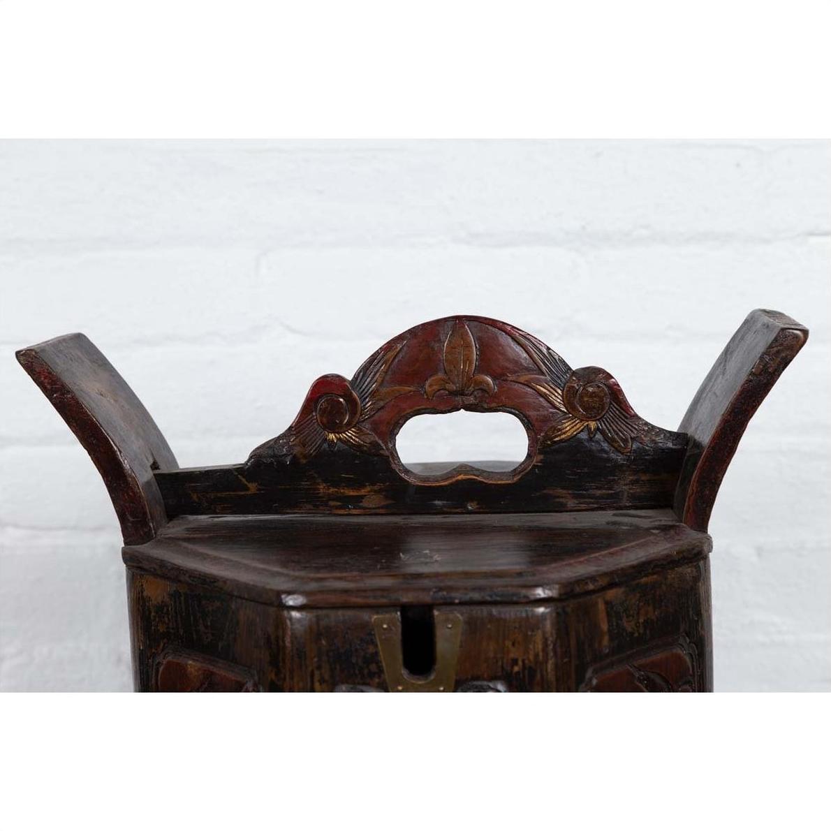 Brown wooden Chinese wedding box with carved handle, animal and foliage motifs, against a white brick wall indoors.