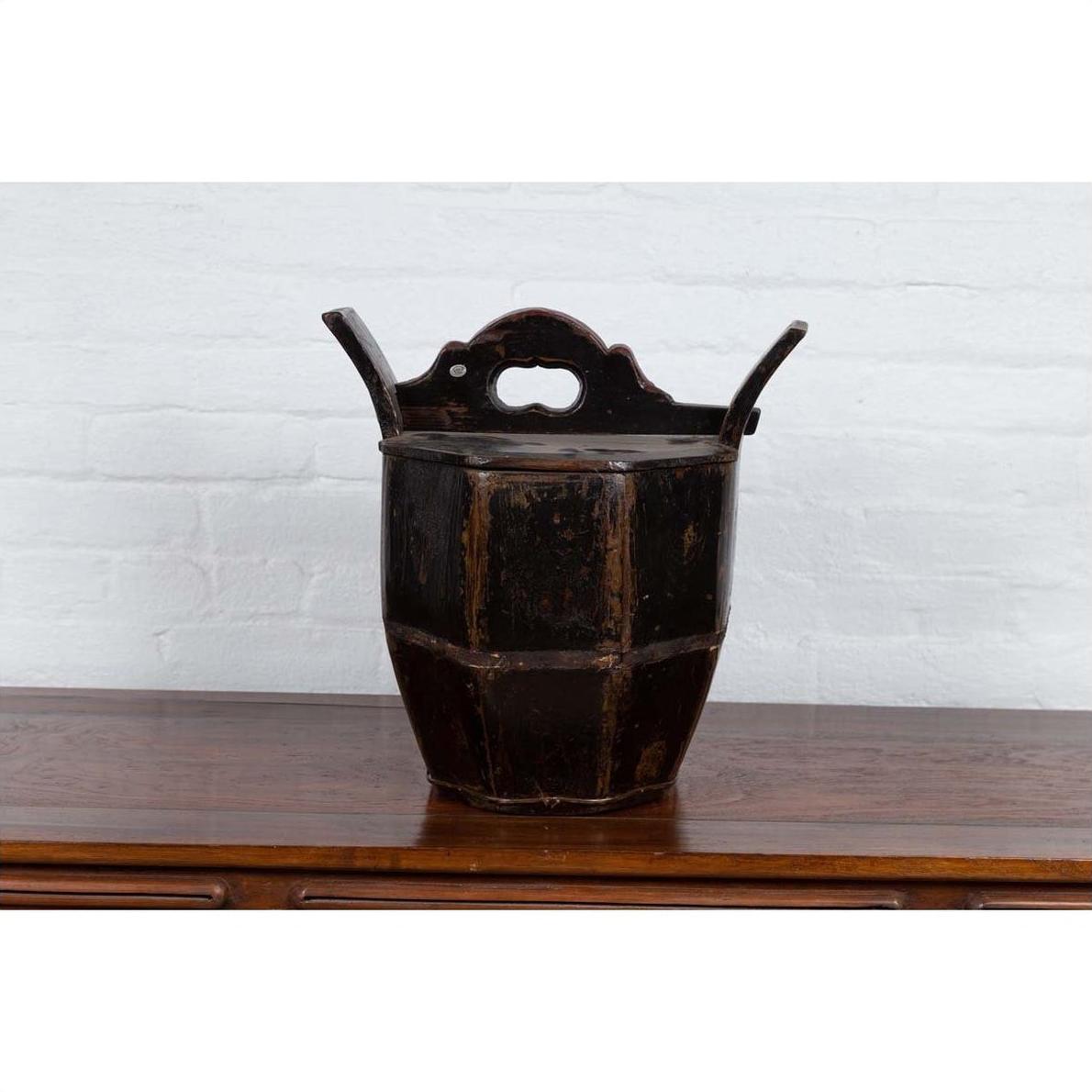 Brown wooden wedding box with carved handle, animal, and foliage motifs on polished surface by a white brick wall.