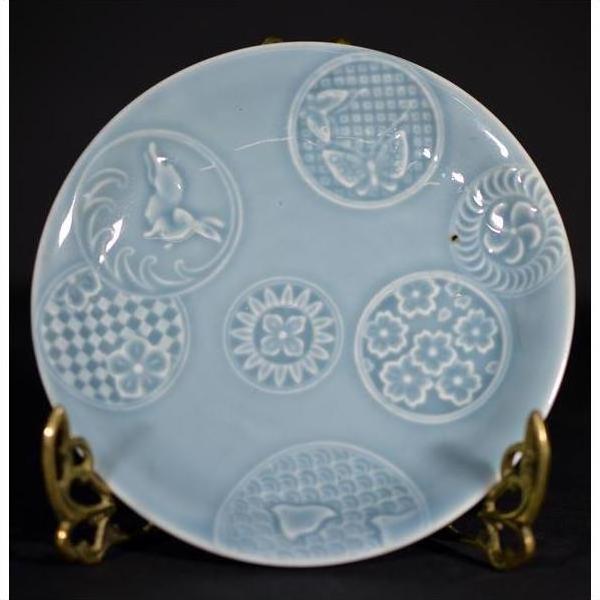 Close-up of an antique white embossed Chinese porcelain plate on a brass stand.