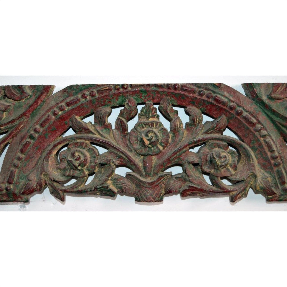 Close-up of antique hand carved wooden mirror frame with intricate floral and leaf designs in dark red and green tones.
