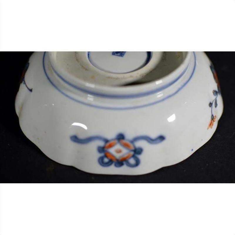 White ceramic bowl base with blue and orange floral motifs and central maker's mark, close-up.