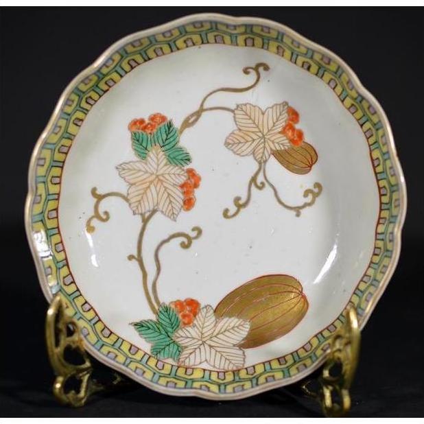 Close-up of an antique hand painted Asian ceramic bowl with floral, green leaf, and orange berry design on metal stand.