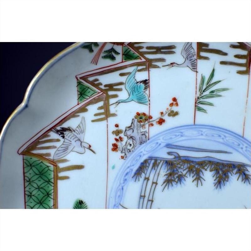 White porcelain plate with hand-painted cranes, green fans, bamboo, and floral accents, close-up view.