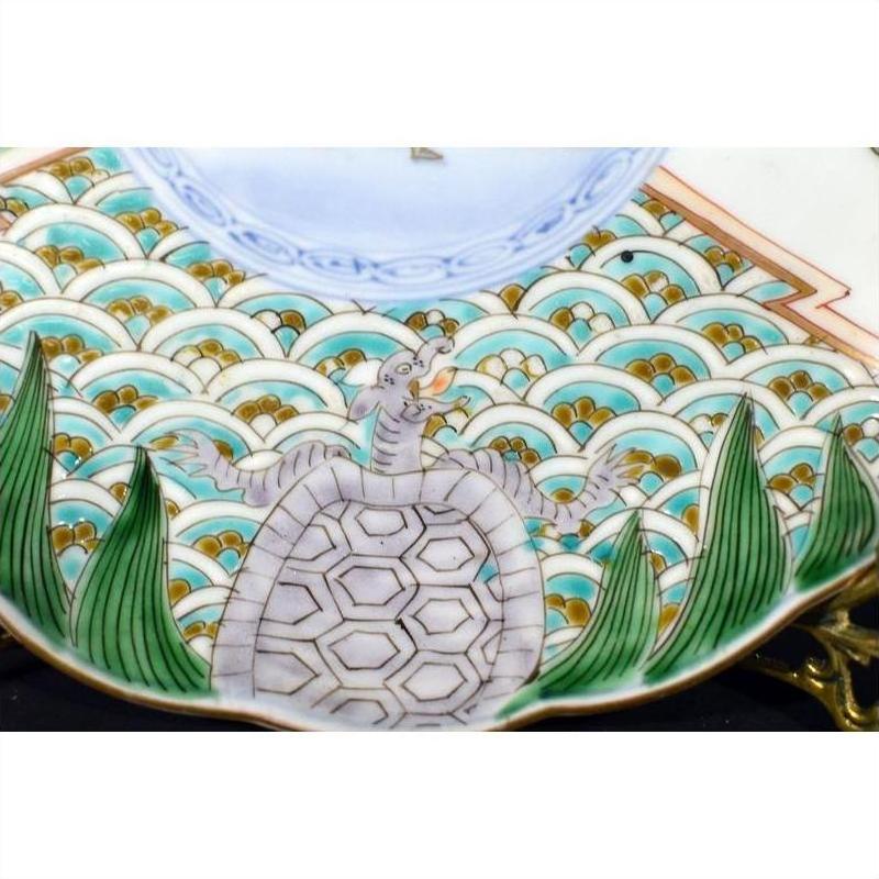 Colorful ceramic plate with turtle and snake design, green leaves, and blue waves on surface.