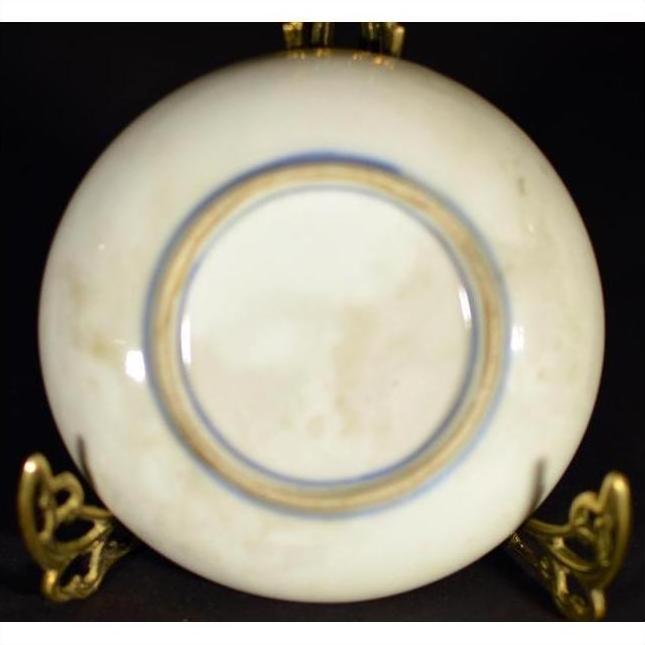 Close-up of antique hand painted Asian plate with blue ring on brass stand against a dark background.